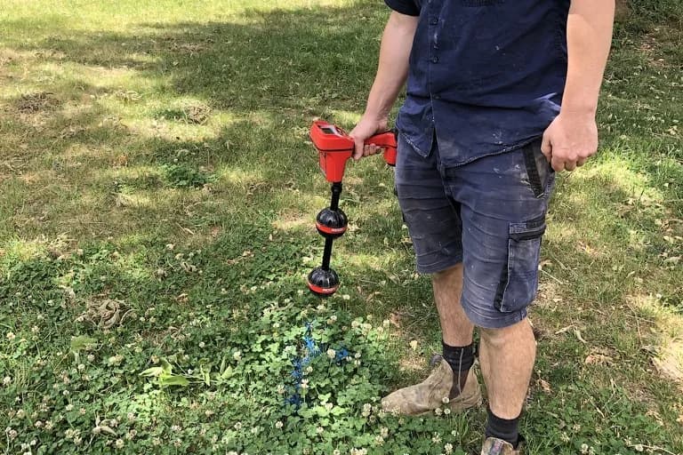 A Fix-It Right plumber using a pipe locator to pinpoint a blocked drain and mark it on the grass above